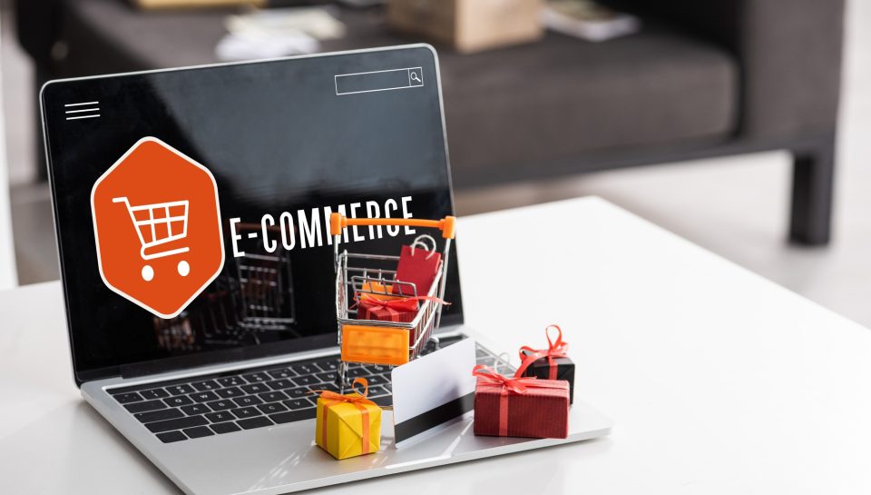 Toy gift boxes and credit card on laptop with e-commerce lettering on table